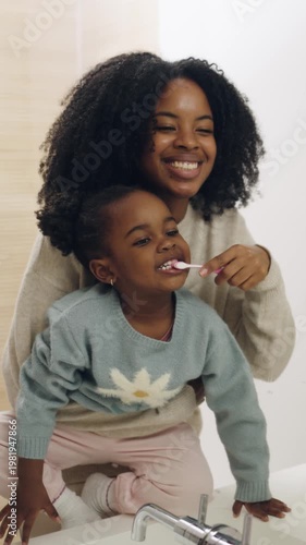 Loving black mother teaching her cute little daughter about dental hygiene. Happy family enjoying their morning routine in the bathroom. Vertical