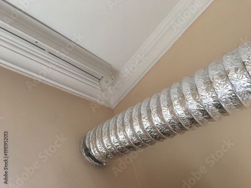 Ventilation duct in corner of room near ceiling showing metal material and installation scene