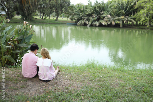 Wide Landscape of Asian Couple Sitting by Lakeside in Public Park
