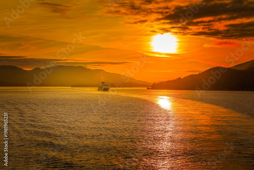 Golden Alaskan fjord sunset with glowing water and the distant silhouette of a passing cruise ship