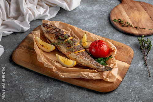 Photos Whole grilled fish served on parchment with lemon wedges, roasted tomato and fre