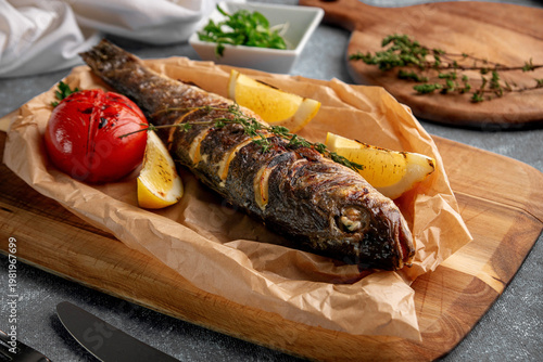 Photos Roasted whole fish with crispy skin served on parchment paper with grilled tomat