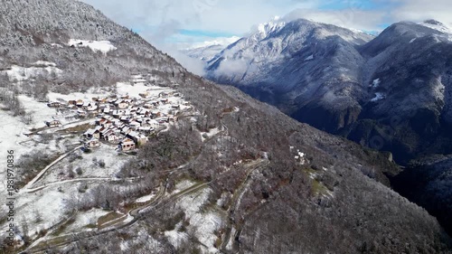 Aerial view of a snowy alpine village with chalets in Tarentaise Valley surrounded by forest and mountains in the French Alps, Savoie, France.