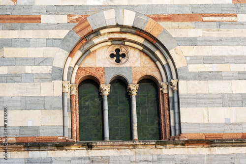 A horizontal view of a Romanesque arched window with three openings and a quatrefoil detail, set within a striking striped marble wall.

