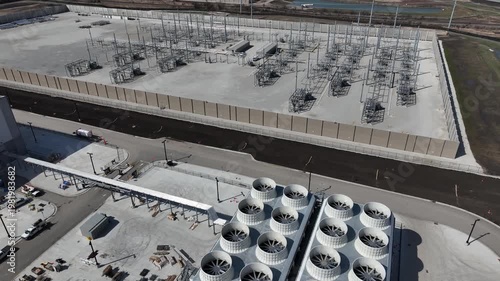 Aerial pan from cooling towers of a data center to a large electrical substation, with another facility under construction in the distance, showcasing power infrastructure for AI and cloud computing.