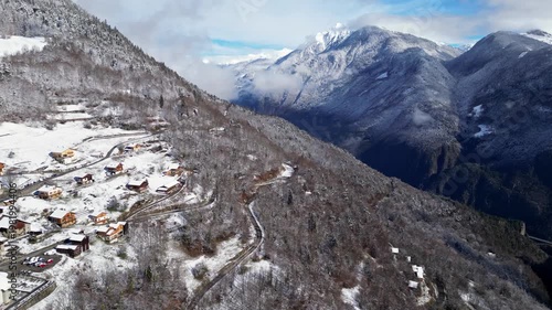 Aerial view of a snowy alpine village with chalets in Tarentaise Valley surrounded by forest and mountains in the French Alps, Savoie, France.