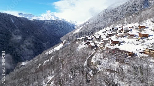 Aerial view of a snowy alpine village with chalets in Tarentaise Valley surrounded by forest and mountains in the French Alps, Savoie, France.