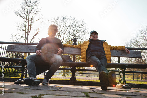 Men sitting on a park bench, enjoying outdoor leisure and relaxation in the sun