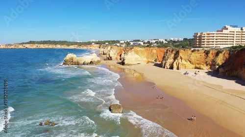 Sunny day on the Algarve coast near Albufeira, Portugal, featuring golden cliffs, sandy beach, and turquoise sea with gentle waves.