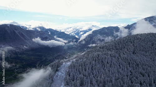 Aerial view of snowy Tarentaise Valley in the French Alps with fog, pine forests and dramatic winter mountains in Savoie, France.