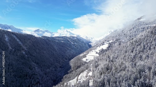 Aerial view of snowy Tarentaise Valley in the French Alps with fog, pine forests and dramatic winter mountains in Savoie, France.