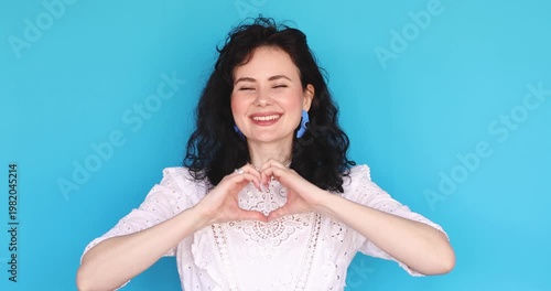 Happy Young Woman Showing Heart Gesture with Hands and Smiling, Charming Female Expressing Love and Gratitude While Looking at Camera, Beautiful Girl Making Heart Symbol on Blue Background