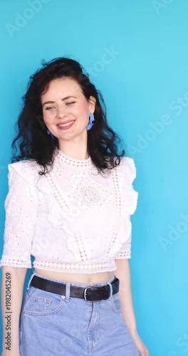 Happy Caucasian Young Woman Smiling and Dancing Freely Isolated on Bright Blue Background, Vertical Portrait of Charming Female with Dark Curly Hair Moving Joyfully to Music