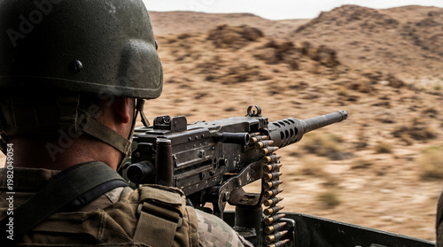 Soldier behind a heavy machine gun on a moving vehicle during a military exercise. Armed man patrolling desert terrain. Combat training and defense strategy in war region.