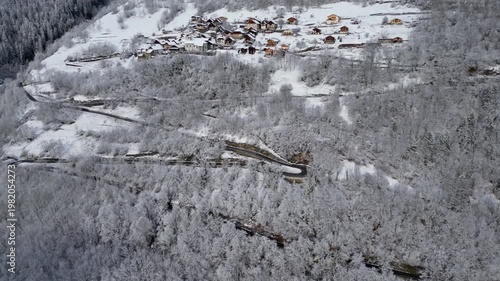 Aerial view of a snowy alpine village with chalets in Tarentaise Valley surrounded by forest and mountains in the French Alps, Savoie, France.