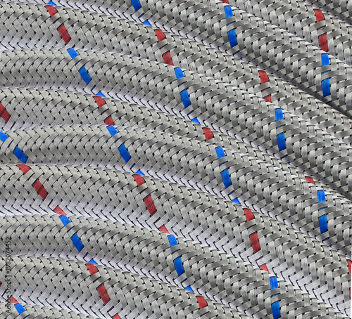 Coiled stainless steel hose with repetitive design woven pattern red, blue stripes. Industrial use, plumbing, maintenance projects. Braided industrial hose texture creating strong geometric background