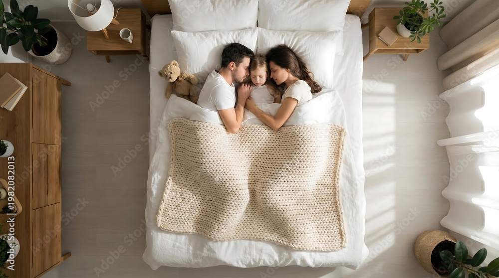 Fototapeta premium Overhead view of a couple lying in bed together, surrounded by wooden furniture and plants in a bright room.