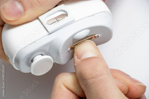 Photos Close-up of hands using electric nail trimmer device with slot, gently filing fingernail length, safe manicure tool for home use, personal nail care concept