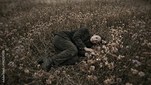 Person lying in a field of dry flowers and plants.