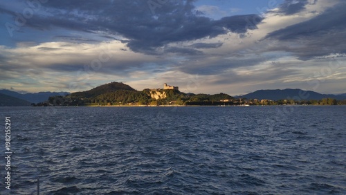 Vászonkép Majestic panoramic view of Rocca di Angera medieval castle on the shores of Lake Maggiore during a dramatic golden hour sunset, Northern Italy
