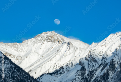 The moon over snow covered Rocky Mountains in Banff Alberta.