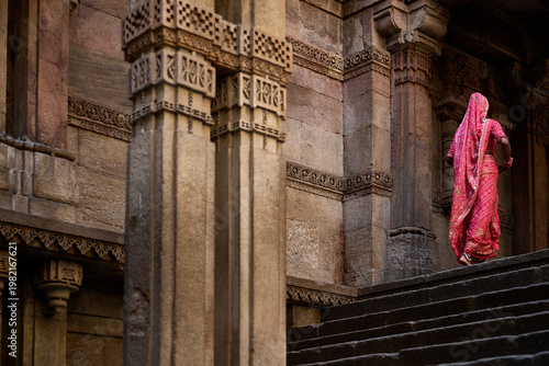 Woman in traditional pink sari walking up stone steps past carved pillars at Adalaj Stepwell, Ahmedabad, Gujarat, India, Asia.