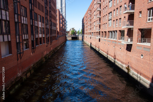 A canal with dark blue water between large red brick warehouses and office buildings in Hamburg's Speicherstadt district
