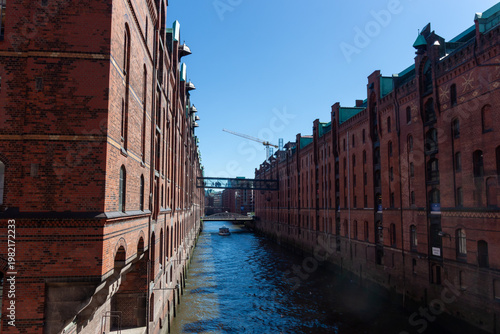 A canal with dark blue water between large red brick warehouses and office buildings in Hamburg's Speicherstadt district