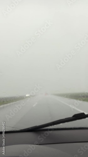 View from inside a car during intense rainstorm with windshield wipers in motion. Wet road and poor visibility create a dangerous driving and safety concept