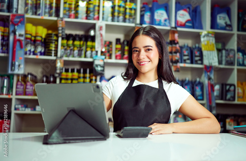 Woman in apron smiling, using a tablet at a counter in an automotive parts store