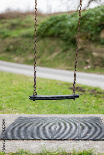 Swing sits empty under gray sky next to road and grass area