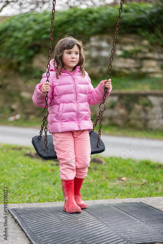 Girl on a swing in a park wearing a pink coat and red boots