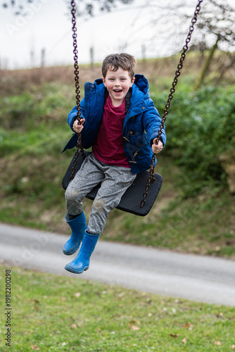 Boy swings joyfully at a playground during a cloudy day