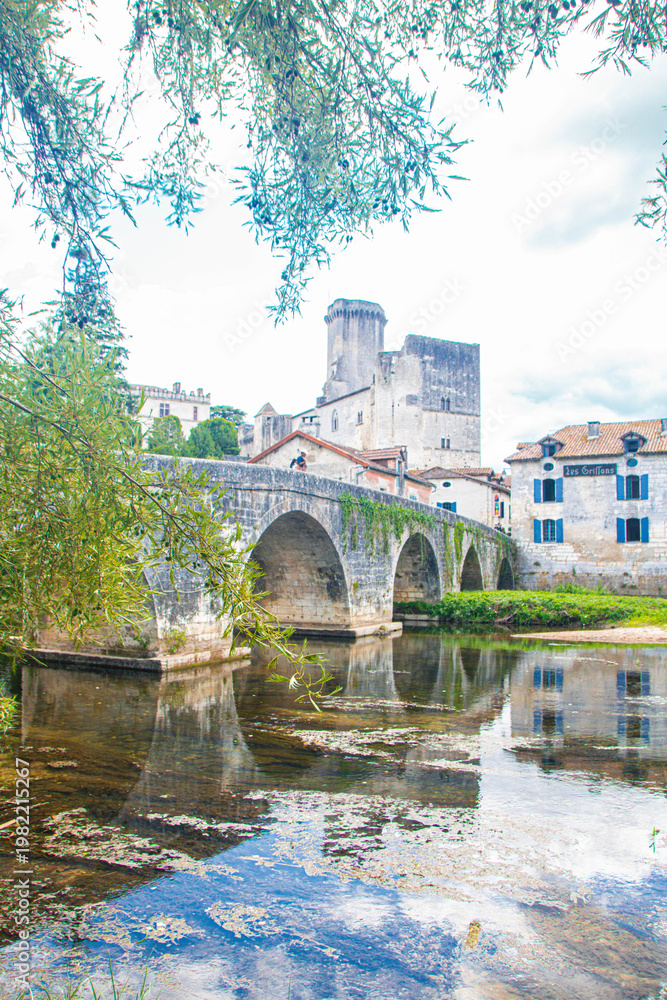 Obraz premium Ancient stone bridge and medieval water mill reflected in the river at Bourdeilles, Dordogne, France. Scenic summer landscape with historic architecture and lush greenery