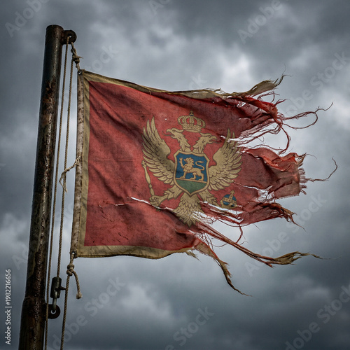 Фотография Torn montenegrin flag flapping on a pole under a stormy sky with waving flag out