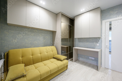 Valokuva cozy room with a mustard-yellow tufted sofa, built-in light beige cabinets, mirr