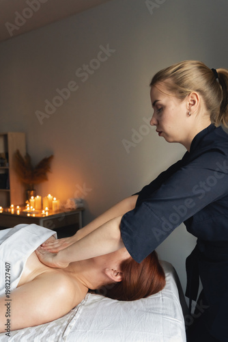 Woman lying on a massage table receiving a professional back and shoulder massage in a relaxing spa environment with candles