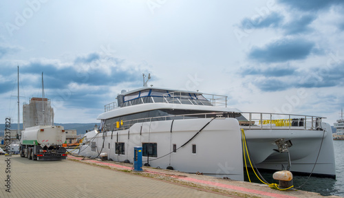 Quadro su tela Modern white power catamaran yacht docked at a pier being refueled by a fuel truck