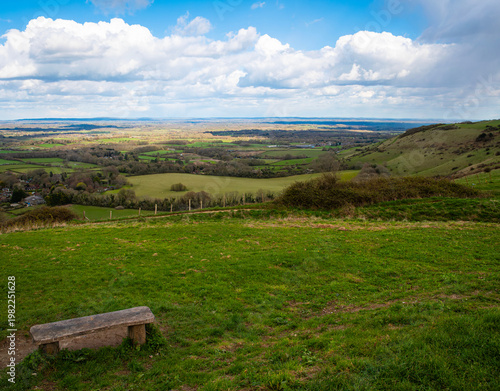 Slika na platnu A wooden bench seat on a green hillside beside the South Downs Way public footpath at Ditchling Beacon, Sussex, overlooking a scenic countryside view of the Sussex Downs