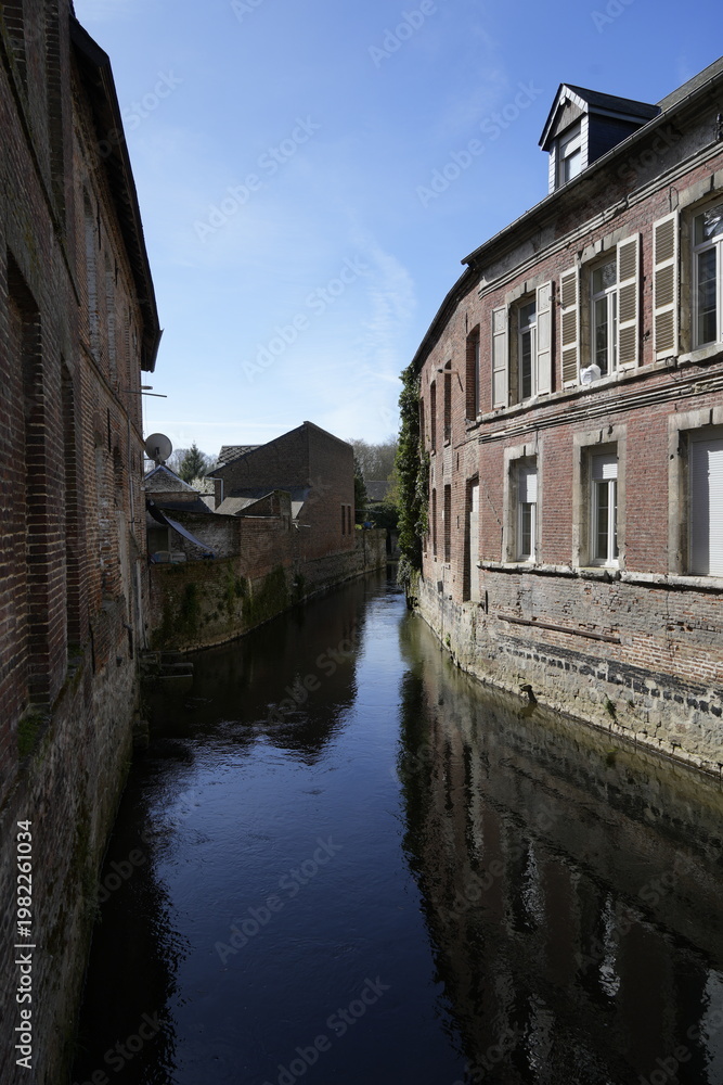 Obraz premium Canal étroit entre de vieilles façades de briques, Guise, Narrow Canal Between Old Brick Facades, Guise