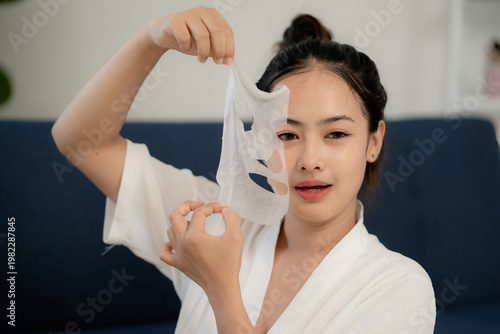 Canvastavla Young Asian woman holding used facial sheet mask after skincare routine at home,