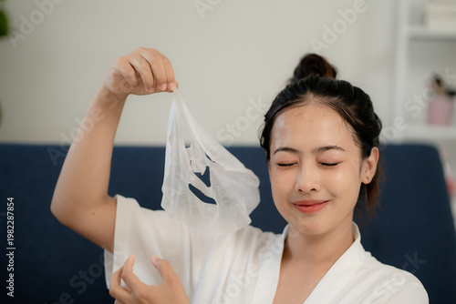 Young Asian woman holding used facial sheet mask after skincare routine at home, glowing skin, beauty treatment concept, self care, cosmetic routine, wellness lifestyle and skincare results