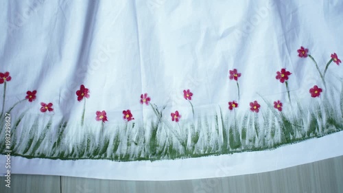 Traditional Bangladeshi hand-painted fabric on a child girl’s white gown with colorful folk art patterns, vibrant textile details, cultural fashion design, and artistic dress decoration.