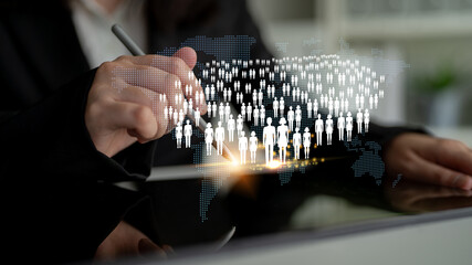 Business professional using digital tablet for global communication and connection with people icons and world map representation in a modern office setting Quark.