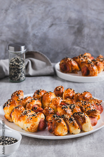 Sausages baked in puff pastry with sesame seeds on a plate on the table vertical view