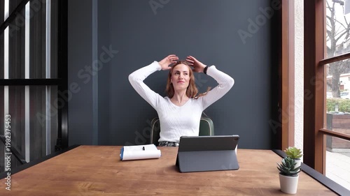 Woman drinking coffee and working on tablet in modern workspace