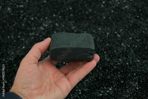 Fotografía Male hand holding black SBR synthetic rubber chunk on black polyethylene granule background