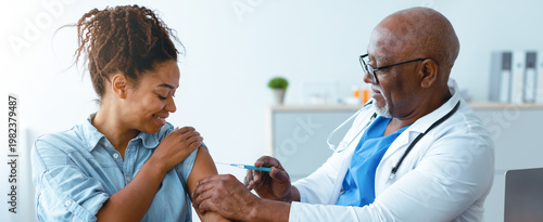 A woman sitting in a clinic smiles as a doctor administers a vaccine to her arm. The doctor wears a stethoscope and looks professional. Soft light fills the room.