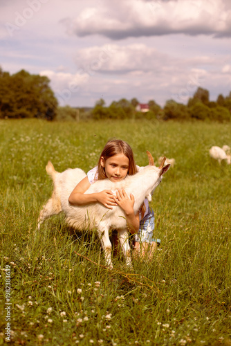 Girl cradling a baby goat in her arms, surrounded by a lush green field, basking in the warmth of a sunny day