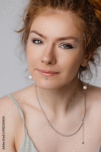 Young Caucasian woman with red hair in bun, green eyes, natural makeup, smiling and looking at camera, white studio background, front view. Beauty, skincare, natural look, positive mood.